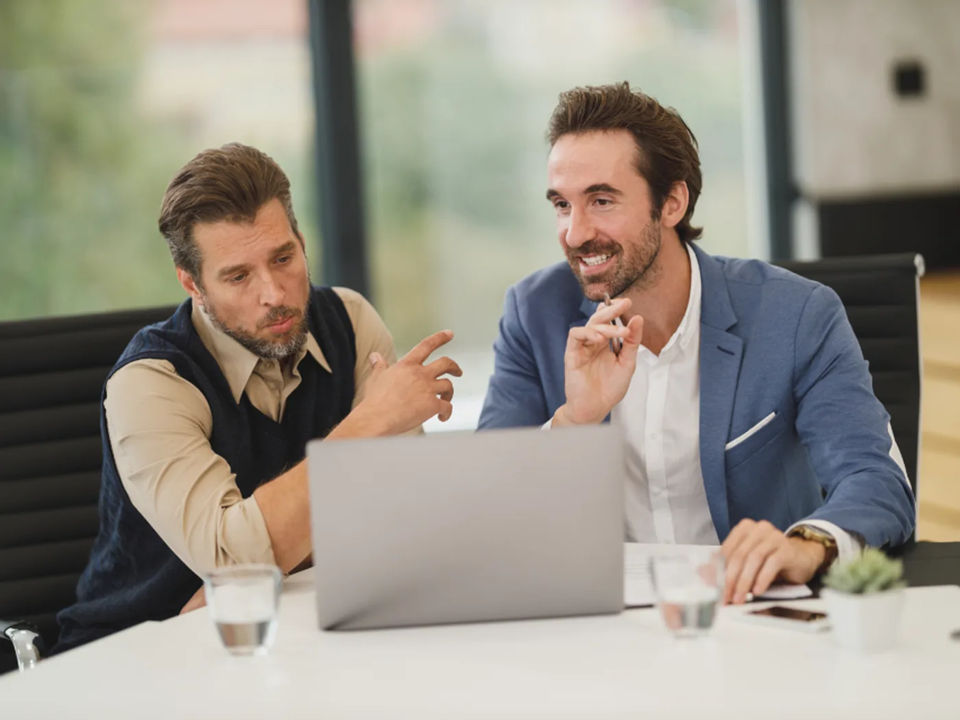 Two colleagues reviewing work together at a laptop in a meeting room.